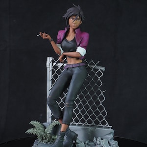 May include: A figurine of a woman in a purple jacket, black top, and distressed black pants, leaning against a chain-link fence. She is holding a cigarette. The figure is on a gray stone base with some greenery.