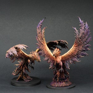 Op de afbeelding: Twee geschilderde miniatuur-phoenix-figuren met uitgespreide vleugels. De phoenixen zijn in een levendige oranje en rode kleur met paarse accenten. Ze staan op ronde bases.