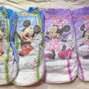 May include: Four disposable training pants featuring Disney characters Mickey Mouse and Minnie Mouse. Two pants have Mickey Mouse on a blue background, and two have Minnie Mouse on a purple background. The training pants are white with green and pink accents.