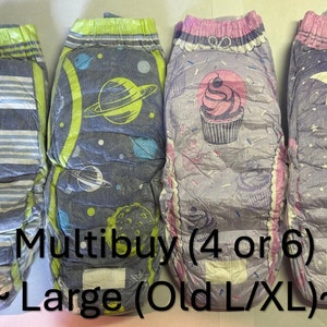 Puede incluir: Cuatro pantalones de entrenamiento para tirar en un paquete múltiple. Los pantalones presentan diferentes diseños: rayas, planetas, magdalenas y estrellas. El texto "Multibuy (4 or 6) ~ Large (Old L/XL) ~" está impreso en la parte inferior de la imagen.