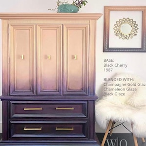 May include: A vintage cabinet with a gradient paint finish, transitioning from a light pink to a dark purple. The cabinet has three doors and two drawers with gold hardware. The cabinet is styled with a white faux fur throw on a chair.