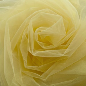 May include: Close-up of a pale yellow tulle fabric arranged in a spiral pattern, resembling a rose. The delicate, sheer material is tightly bunched, creating a textured, layered effect. Ideal for crafting, this fabric offers a soft, airy aesthetic.