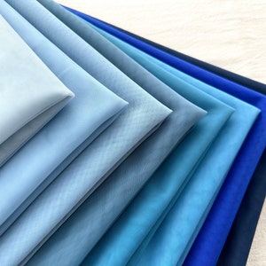May include: A stack of blue and navy blue fabric swatches, arranged in a gradient from light blue to dark blue.