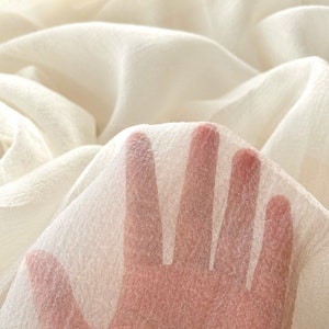 Puede incluir: Primer plano de una mano descansando sobre una tela blanca transparente. La tela tiene una superficie ligeramente texturizada.