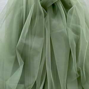 May include: A piece of sage green tulle fabric, draped and folded, showing the sheer, delicate texture of the material.