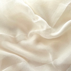 Puede incluir: Primer plano de una tela blanca transparente con una textura suave y fluida. La tela est&aacute; drapeada y doblada, creando un aspecto suave y elegante.
