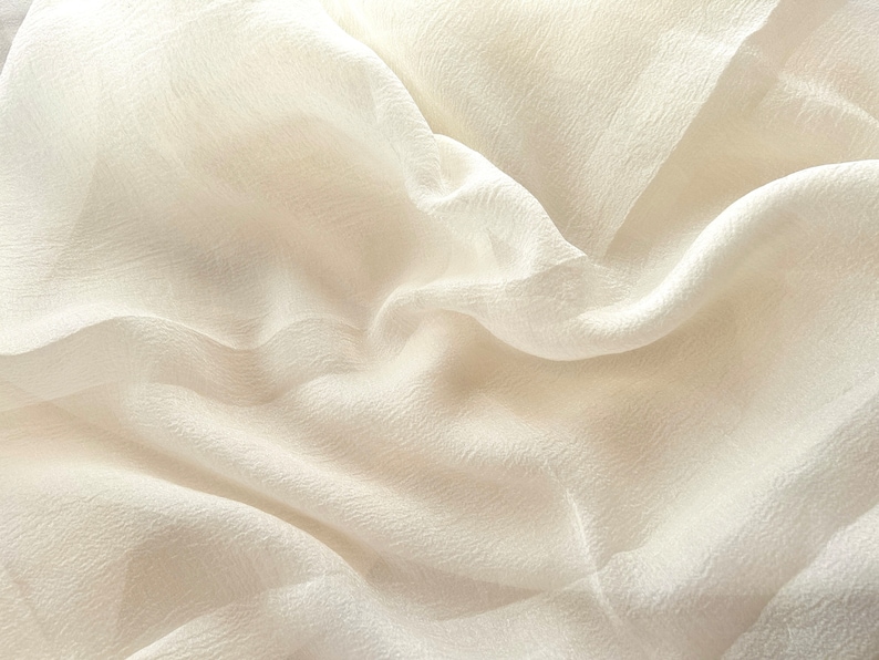 Puede incluir: Primer plano de una tela blanca transparente con una textura suave y fluida. La tela est&aacute; drapeada y doblada, creando un aspecto suave y elegante.