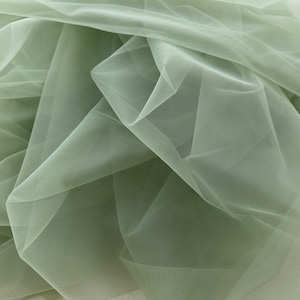 May include: A close-up of a sage green tulle fabric. The fabric is soft and sheer, with a delicate texture.