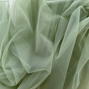 May include: A piece of soft, sage green tulle fabric. The fabric is sheer and delicate, with a slightly crinkled texture.