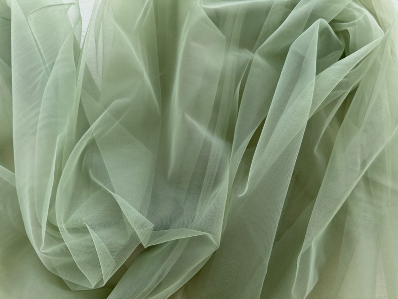 May include: A piece of soft, sage green tulle fabric. The fabric is sheer and delicate, with a slightly crinkled texture.