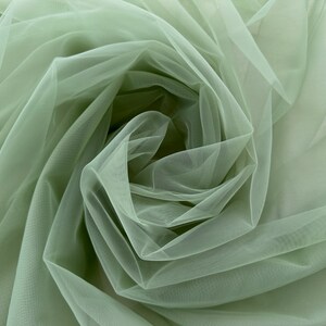 May include: A close-up of sage green tulle fabric, showing the soft, delicate texture and the way it drapes and folds.