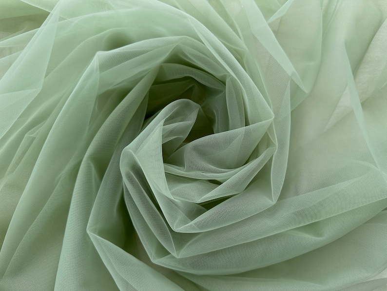 May include: A close-up of sage green tulle fabric, showing the soft, delicate texture and the way it drapes and folds.