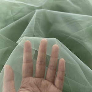 May include: A piece of soft, sage green tulle fabric. The fabric is sheer and delicate, with a fine mesh weave.