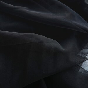 May include: Close-up of black tulle fabric with a soft, flowing texture. The fabric is gathered and draped, creating a delicate and airy look.