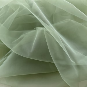 May include: A piece of soft, sage green tulle fabric. The fabric is sheer and delicate, with a slightly crinkled texture.