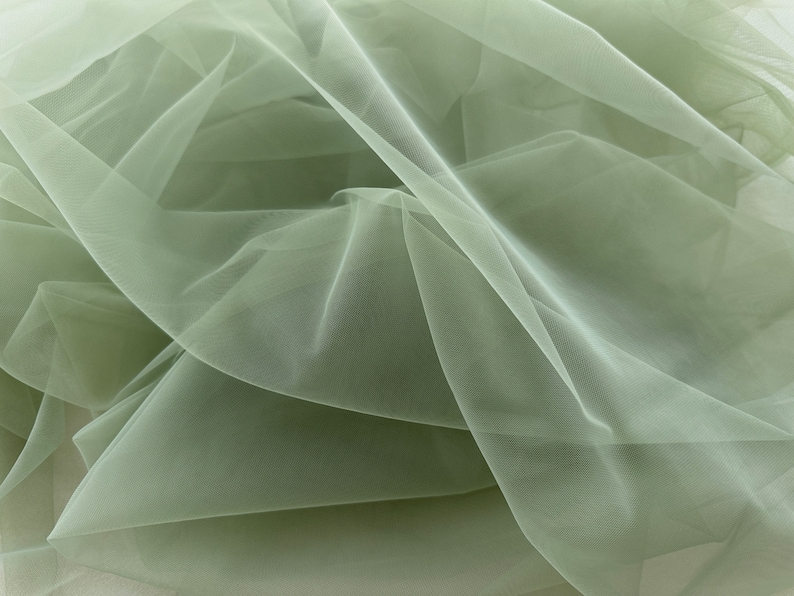May include: A piece of soft, sage green tulle fabric. The fabric is sheer and delicate, with a slightly crinkled texture.