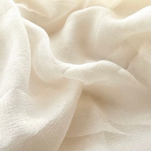 Puede incluir: Una tela blanca y transparente con una superficie texturizada. La tela est&aacute; drapeada y doblada, creando pliegues y curvas suaves.