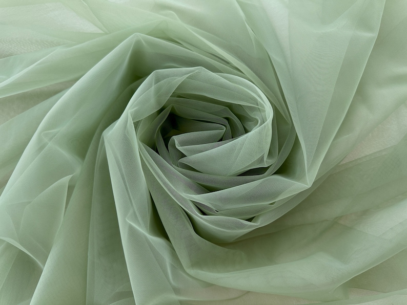 May include: A close-up of a sage green tulle fabric, showing the soft, delicate texture and the way it drapes.