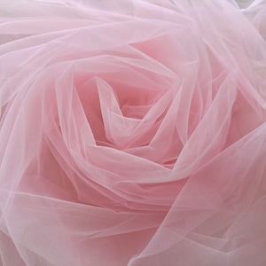 以下が含まれることがあります： 柔らかくピンク色のチュール生地のクローズアップ。ドレープされ、集められて、繊細で渦巻くパターンが作られています。