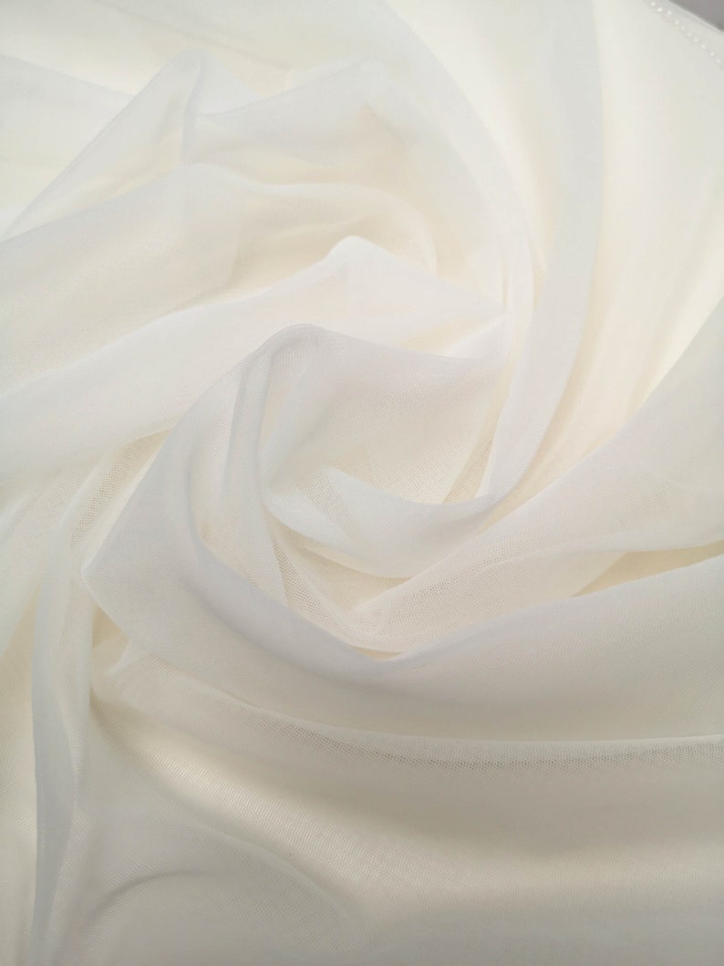 May include: White sheer fabric with a soft, flowing texture. The fabric is draped and folded, creating a smooth, elegant look.