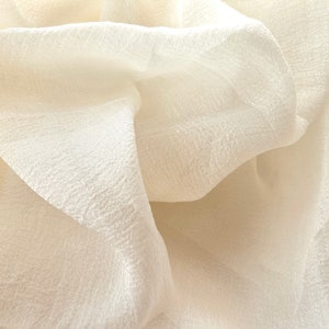 Puede incluir: Primer plano de una tela suave y blanca con una superficie texturizada. La tela est&aacute; drapeada y doblada, creando un aspecto suave y fluido.