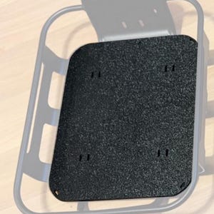 May include: A gray metal rack with a black textured plate. The plate has rounded corners and several small holes. The rack has a curved top and a rectangular base, likely for mounting.
