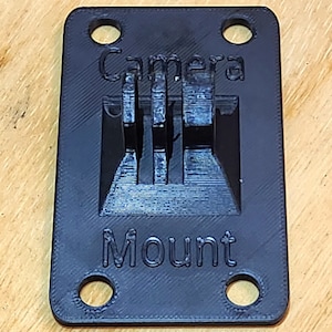 May include: A black 3D printed camera mount with four holes and the text "Camera Mount" printed on it.
