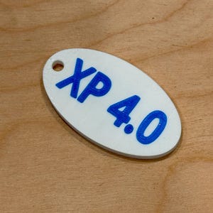 May include: White oval tag with the text "XP 4.0" in blue. The tag has a small hole at the top. The tag is on a wooden surface.