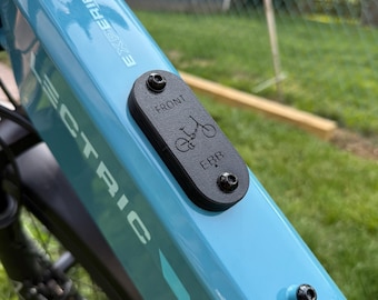 Puede incluir: Primer plano del cuadro azul claro de una bicicleta eléctrica. La palabra "EXPERIENCE" está impresa en blanco. Una placa negra con "FRONT" y un gráfico de bicicleta está adjunta. También es visible la palabra "ELECTRIC".