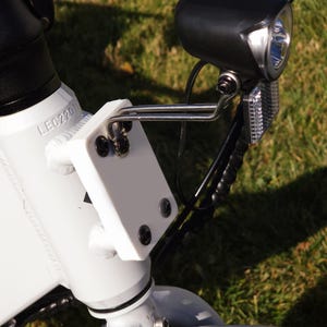 May include: Close-up of a white electric bicycle with a black headlight and a white plastic bracket. The bracket has the text "LEC220" printed on it.