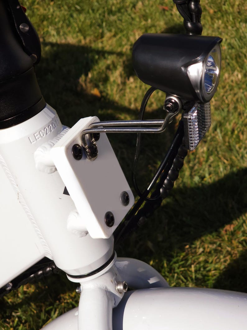 May include: Close-up of a white electric bicycle with a black headlight and a white plastic bracket. The bracket has the text "LEC220" printed on it.