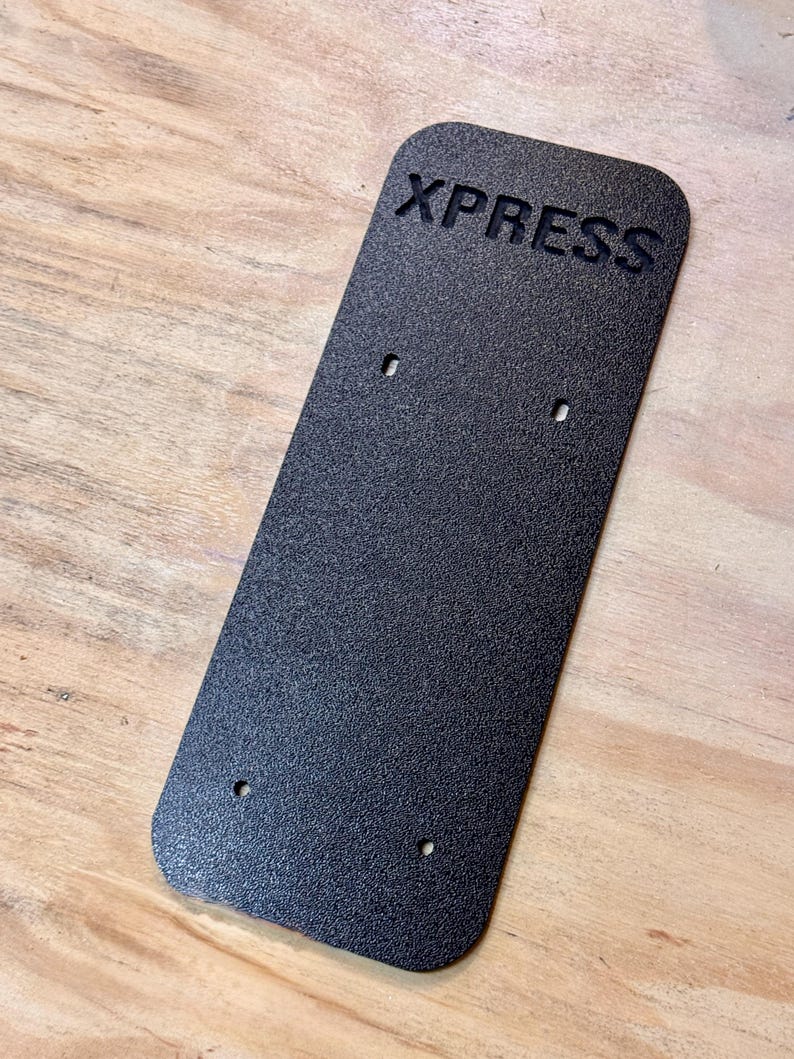May include: A black rectangular sign with the word "XPRESS" embossed in white letters. The sign has four small holes drilled into it.