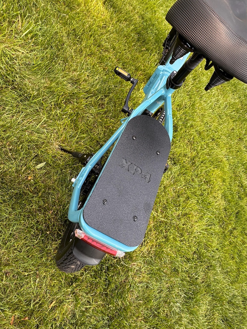 May include: A light blue electric scooter with a black seat and footboard. The footboard has the text "XP4" printed on it. The scooter is on a grassy surface.