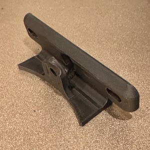May include: A 3D printed black plastic mount with two holes on the top and a curved base.
