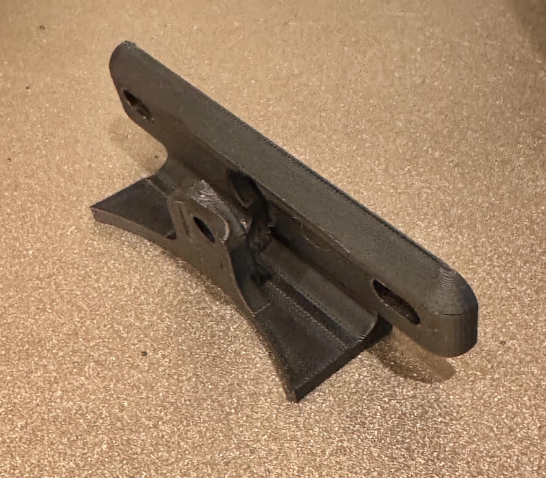 May include: A 3D printed black plastic mount with two holes on the top and a curved base.