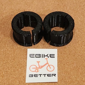 Op de afbeelding: Twee zwarte plastic kabelklemmen met een getextureerd oppervlak. De klemmen zijn ontworpen om kabels op hun plaats te houden.