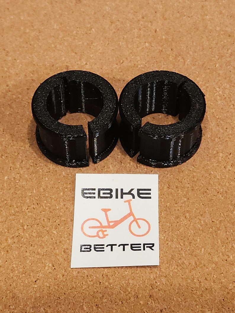 Op de afbeelding: Twee zwarte plastic kabelklemmen met een getextureerd oppervlak. De klemmen zijn ontworpen om kabels op hun plaats te houden.