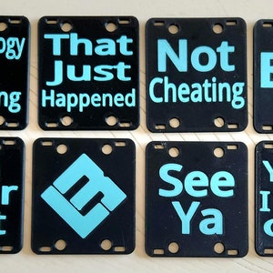 May include: Eight black square tiles with rounded corners and white text on a light wood surface. The text on the tiles reads: "Technology Isn't Cheating", "That Just Happened", "Not Cheating", "Bye", "On Your Left", "See Ya", "Yeah, I Don't Care".