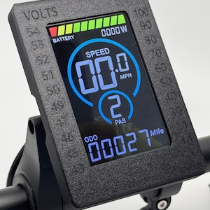 May include: Black electric bike display with a digital speedometer showing 00.0 mph, a battery level indicator, and an odometer reading 00027 miles. The display also shows a PAS level of 2.