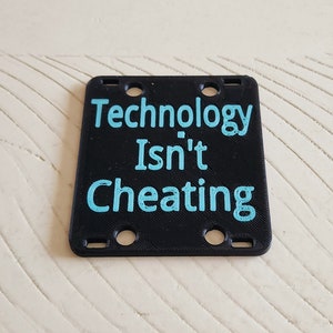 May include: Black square sign with rounded corners and six holes. The sign has the text "Technology Isn't Cheating" in light blue.