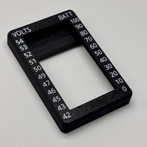 May include: A black rectangular gauge with white text indicating voltage and battery levels. The gauge reads "VOLTS" and "BATT" with numerical values from 0 to 100. The text "ALES FROM" is also visible.