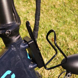 May include: Black bicycle with a black water bottle holder attached to the frame. The bicycle has a blue and white logo on the frame.