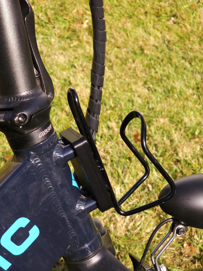 May include: Black bicycle with a black water bottle holder attached to the frame. The bicycle has a blue and white logo on the frame.