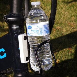 May include: A black bicycle water bottle holder with a clear plastic water bottle inside. The bottle has a blue and white label that reads "Great Value Purified Drinking Water".