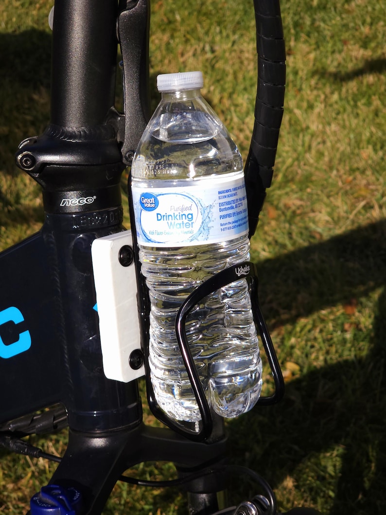 May include: A black bicycle water bottle holder with a clear plastic water bottle inside. The bottle has a blue and white label that reads "Great Value Purified Drinking Water".