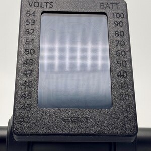 May include: A black electric scooter display with a digital screen showing the battery level and voltage. The display reads "VOLTS" and "BATT" with numbers ranging from 43 to 54 for volts and 10 to 100 for battery.
