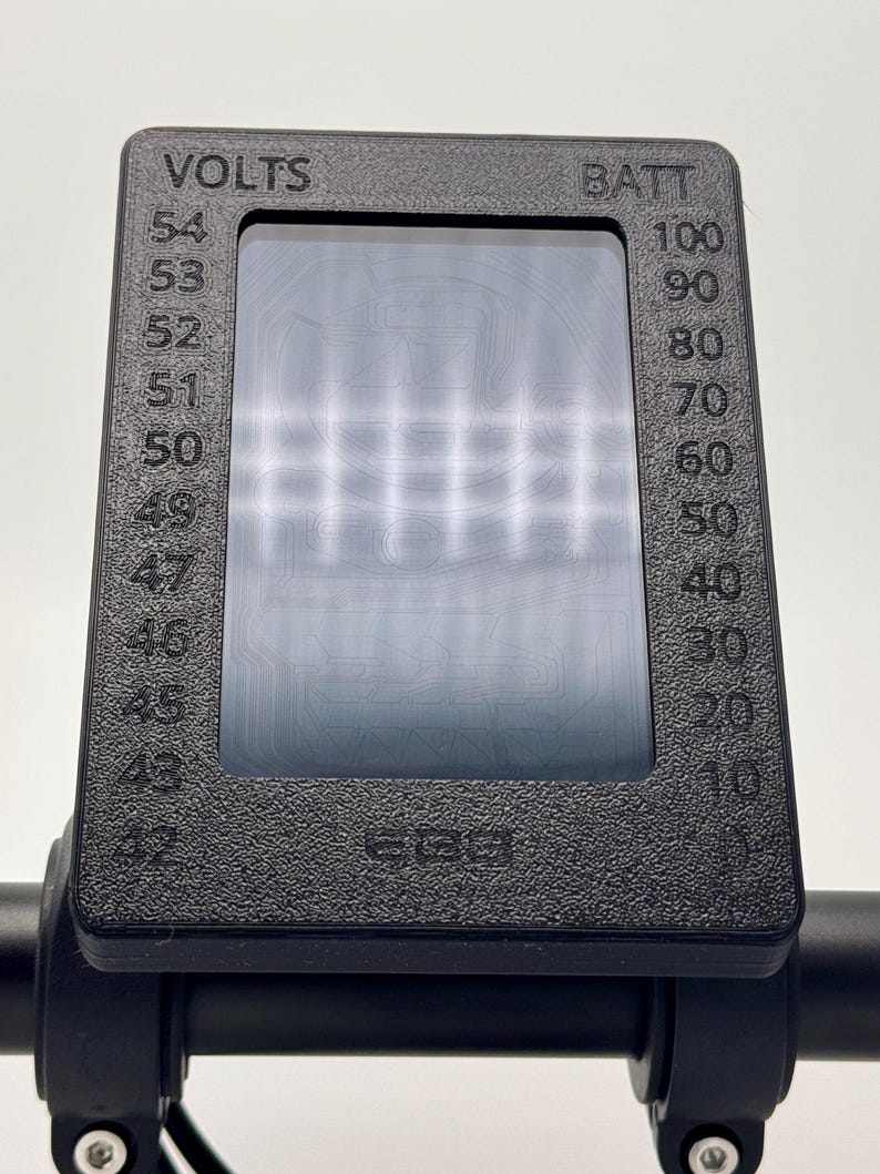 May include: A black electric scooter display with a digital screen showing the battery level and voltage. The display reads "VOLTS" and "BATT" with numbers ranging from 43 to 54 for volts and 10 to 100 for battery.