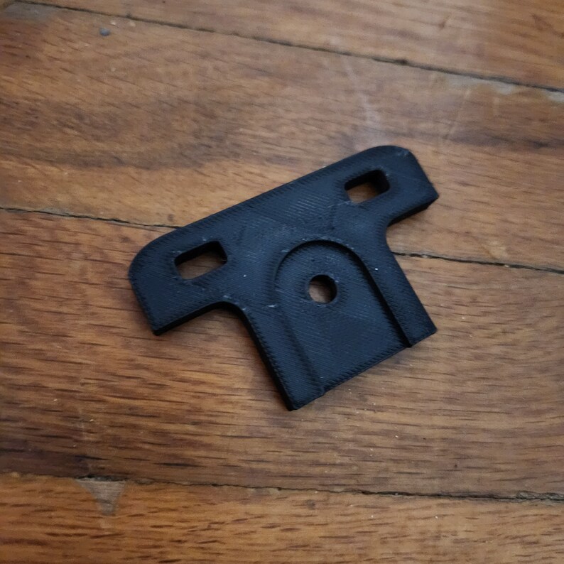 May include: A black plastic T-shaped bracket with two holes on each side and a circular hole in the center.