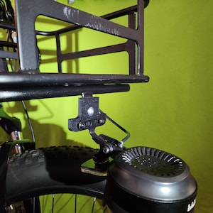 May include: A black metal bike rack with a black metal bracket attached to the bottom. The bracket is attached to a black electric bike motor.
