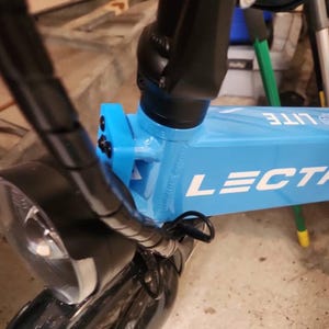 May include: A close-up of a blue electric bike with black handlebars and a black headlight. The bike has the word "LECTRA LITE" printed on the frame.